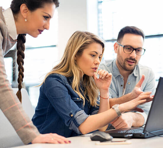 Group of 3 discussing in front of a laptop